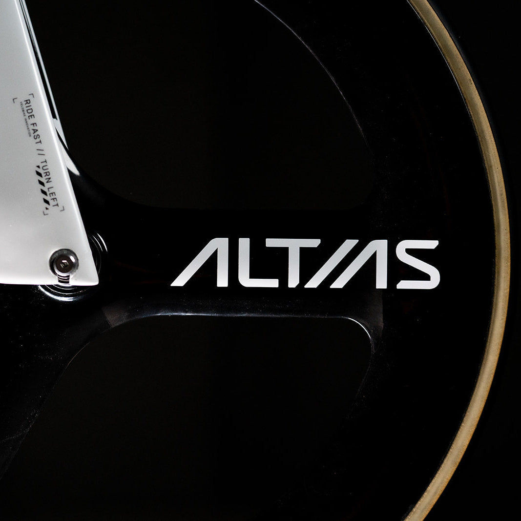 Close-up of a black bicycle wheel with a silver aluminum fork and the white ALTIAS brand logo on the frame, set against a dark background.